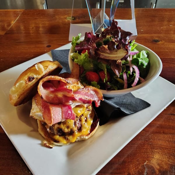A Hawk N Dove burger with melted cheese, bacon, and a fried egg, served with a side salad.