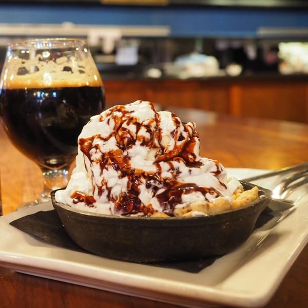 Skillet cookie with whipped cream and chocolate drizzle next to a dark beer at Hawk N Dove.