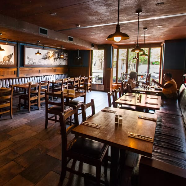 Warmly lit interior of Hawk N Dove restaurant with wooden tables, booth seating, and animal artwork.