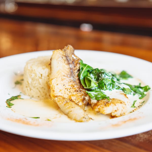 Pan-seared fish with rice, creamy sauce, and spinach on a white plate at Hawk N Dove.