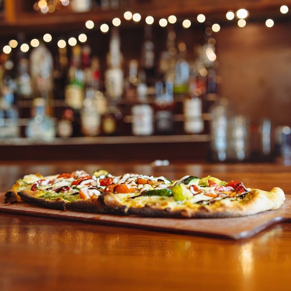 Hawk N Dove's flatbread pizza with pesto, tomatoes, and cheese on a wooden bar.