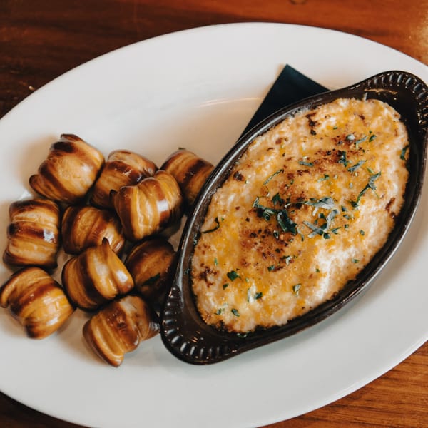 Hawk N Dove's creamy mac and cheese with crispy bacon-wrapped tots on a white plate.
