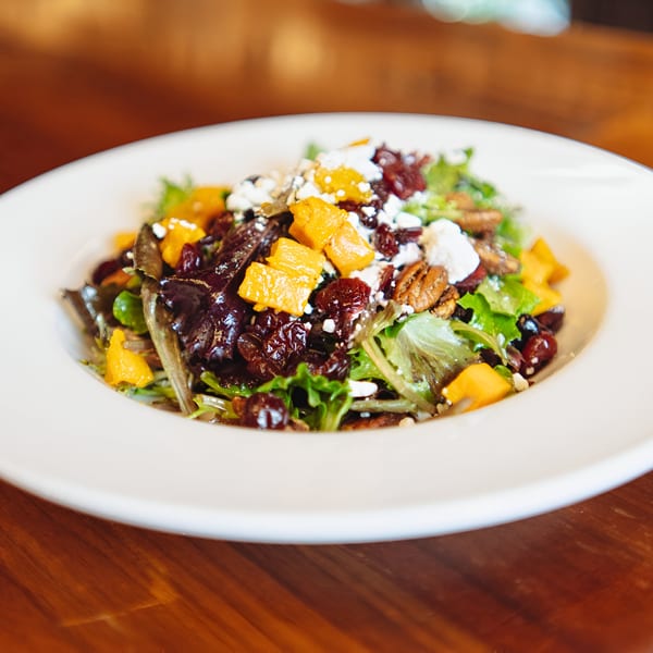 A vibrant salad with mixed greens, orange chunks, dried cranberries, pecans, and feta cheese.