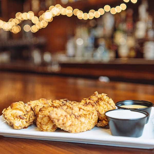 Crispy fried chicken tenders with two dipping sauces on a white plate at Hawk N Dove.