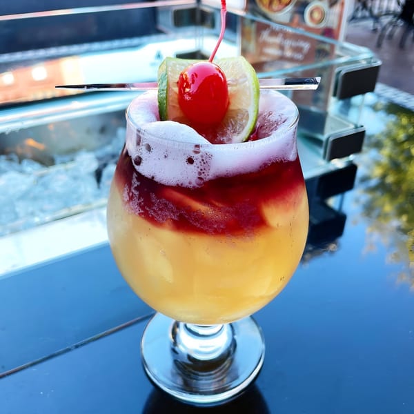 A colorful cocktail with yellow and red layers, topped with foam, lime, and a cherry.