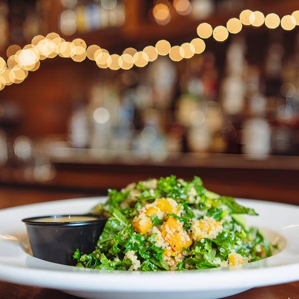 A vibrant kale and quinoa salad with butternut squash, served with dressing at Hawk N Dove.
