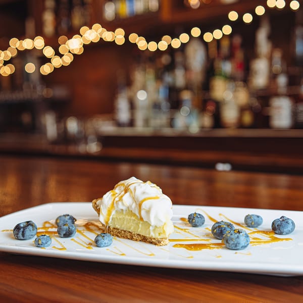 A slice of pie with whipped cream, caramel drizzle, and blueberries on a white plate.