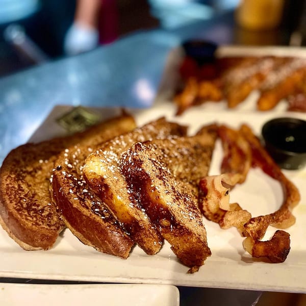 Hawk N Dove's French toast dusted with powdered sugar and cinnamon, served with crispy bacon.